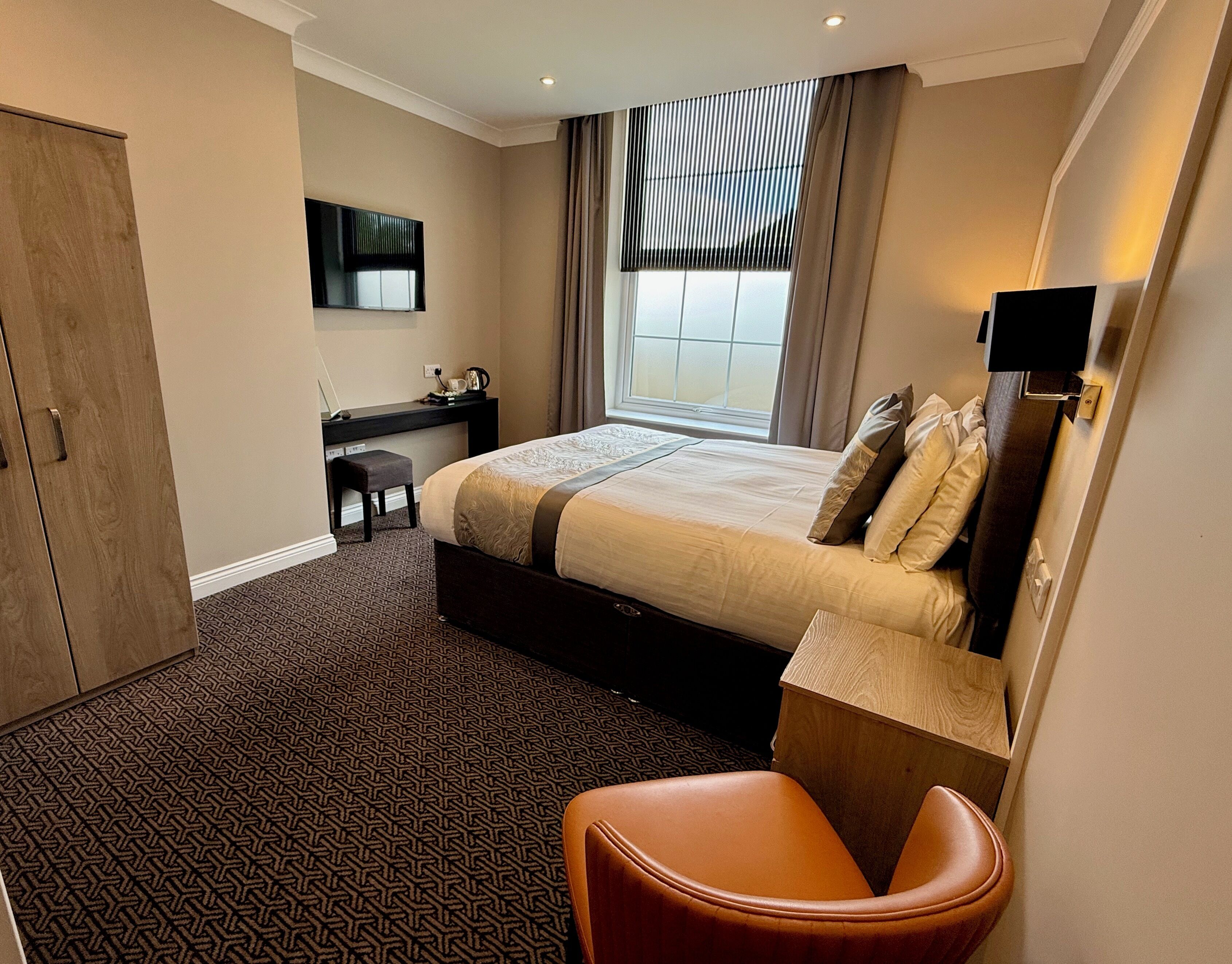 Ein Hotelzimmer mit Bett, Schreibtisch, Stuhl, Kleiderschrank und einem Fenster mit Vorhängen.