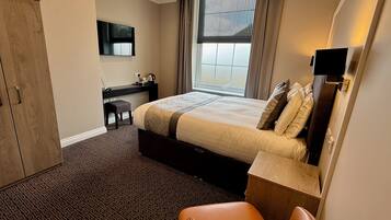 Ein Hotelzimmer mit Bett, Schreibtisch, Stuhl, Kleiderschrank und einem Fenster mit Vorhängen.