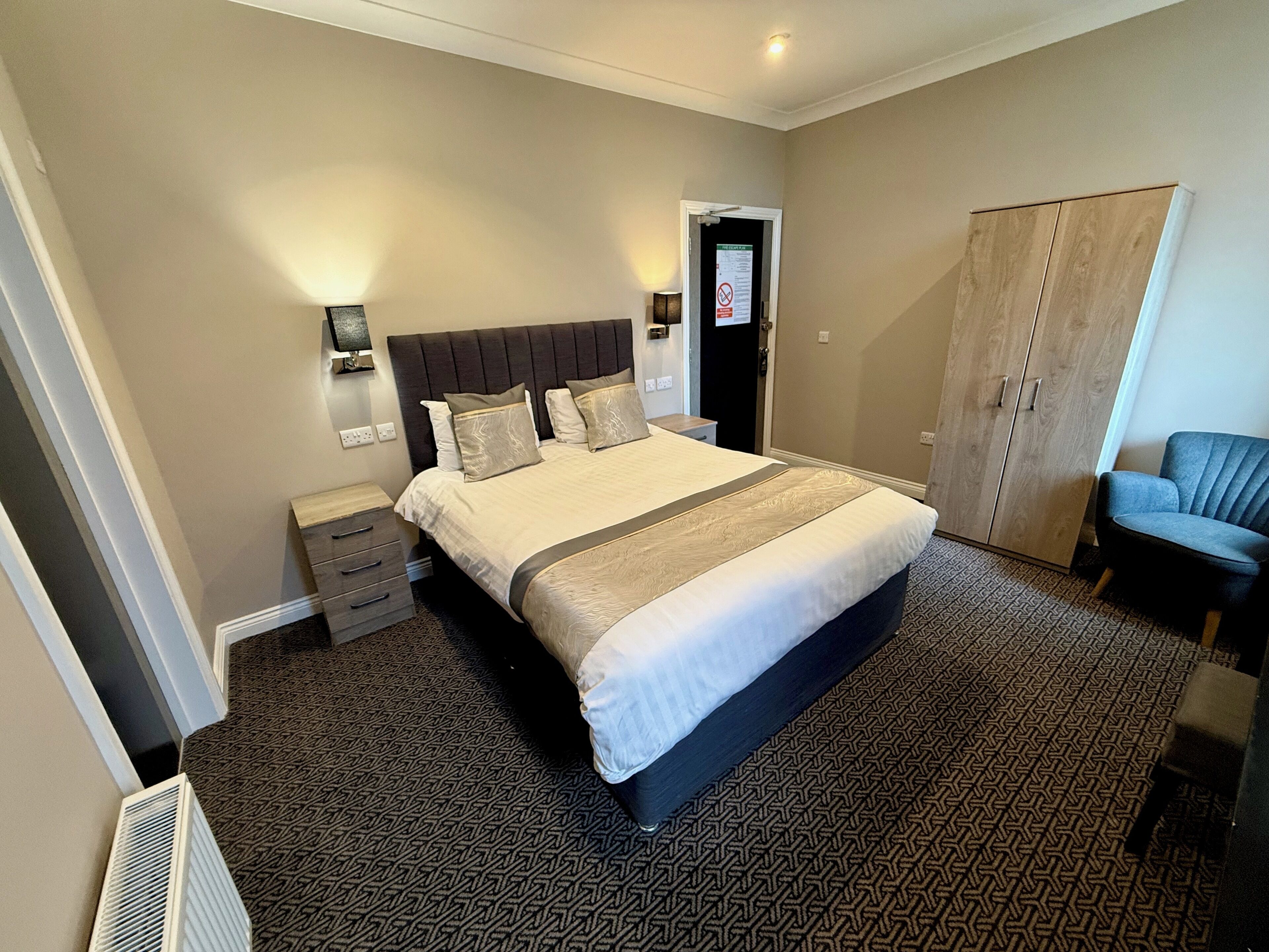 A hotel room with a large bed, bedside tables, a wardrobe, and a chair.
