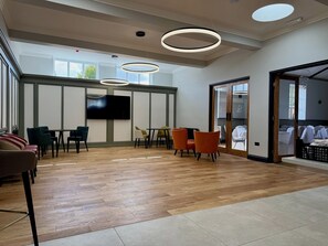 A modern hotel room with a wooden floor, a flat-screen TV, and a seating area with chairs and tables. - The Raven Hotel - Inn (Corby)