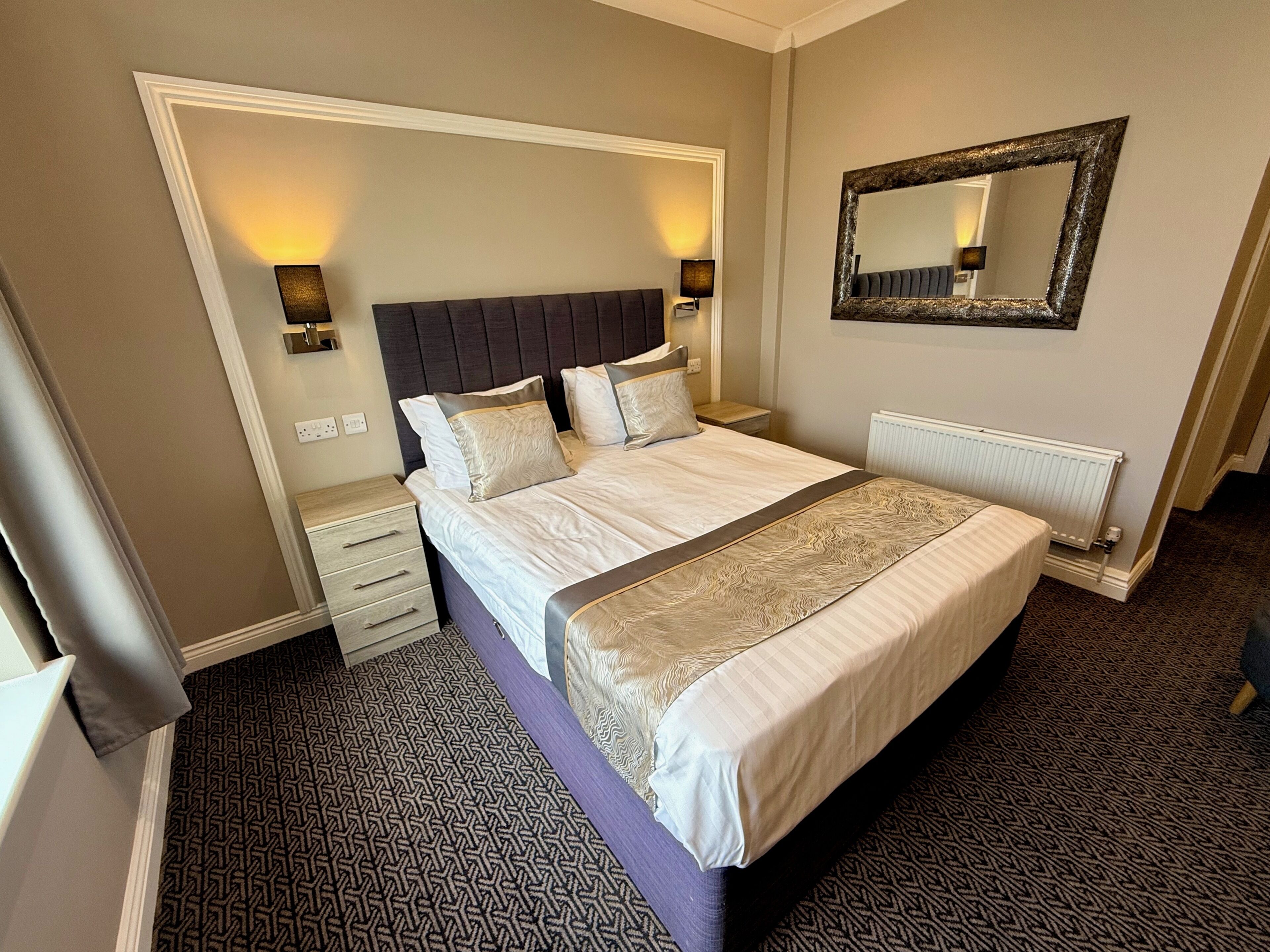 A hotel room with a large bed, bedside lamps, a mirror, and a radiator.
