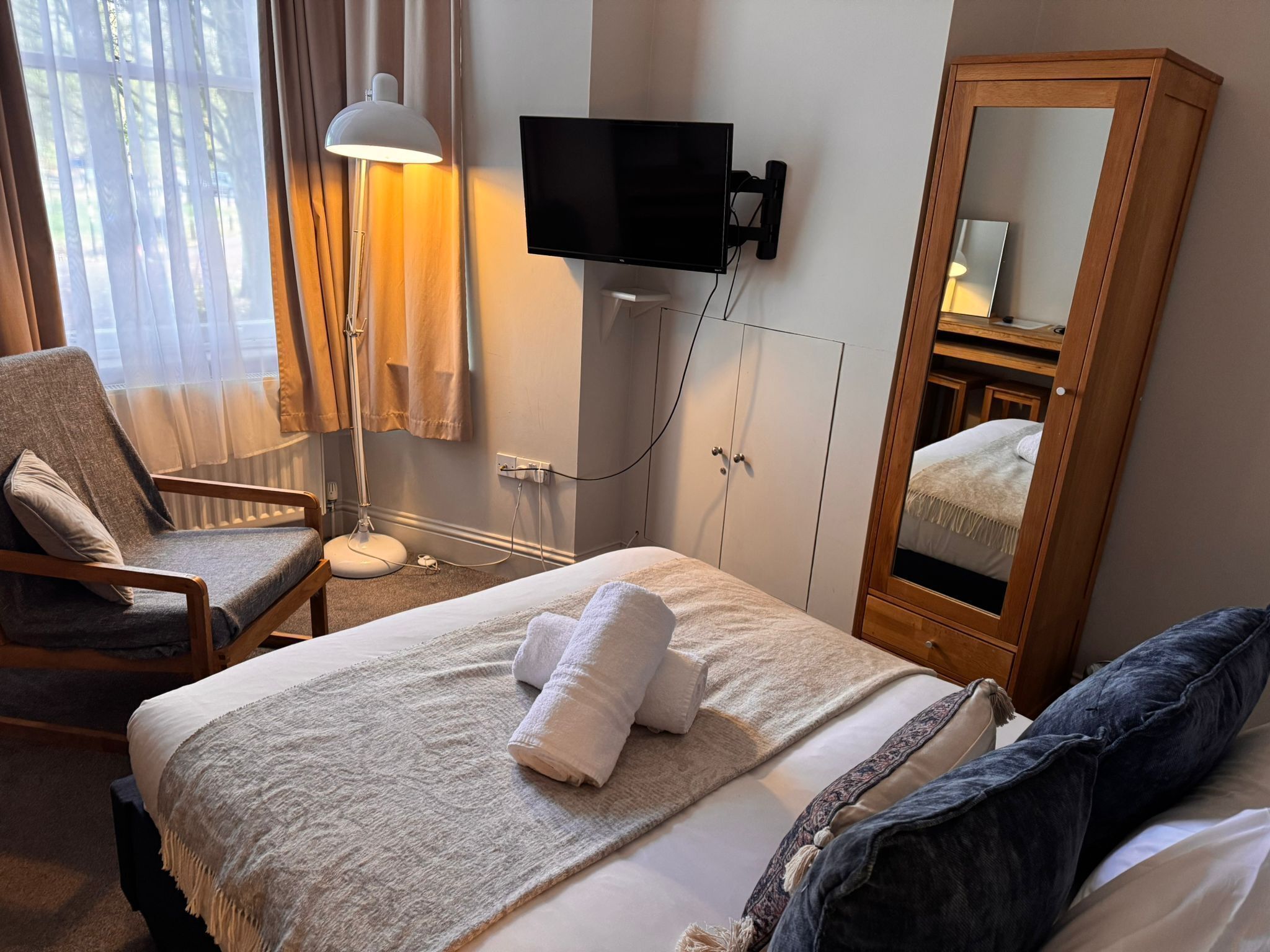 Ein Hotelzimmer mit Bett, Sessel, Wand-Fernseher, Kleiderschrank und Spiegel.