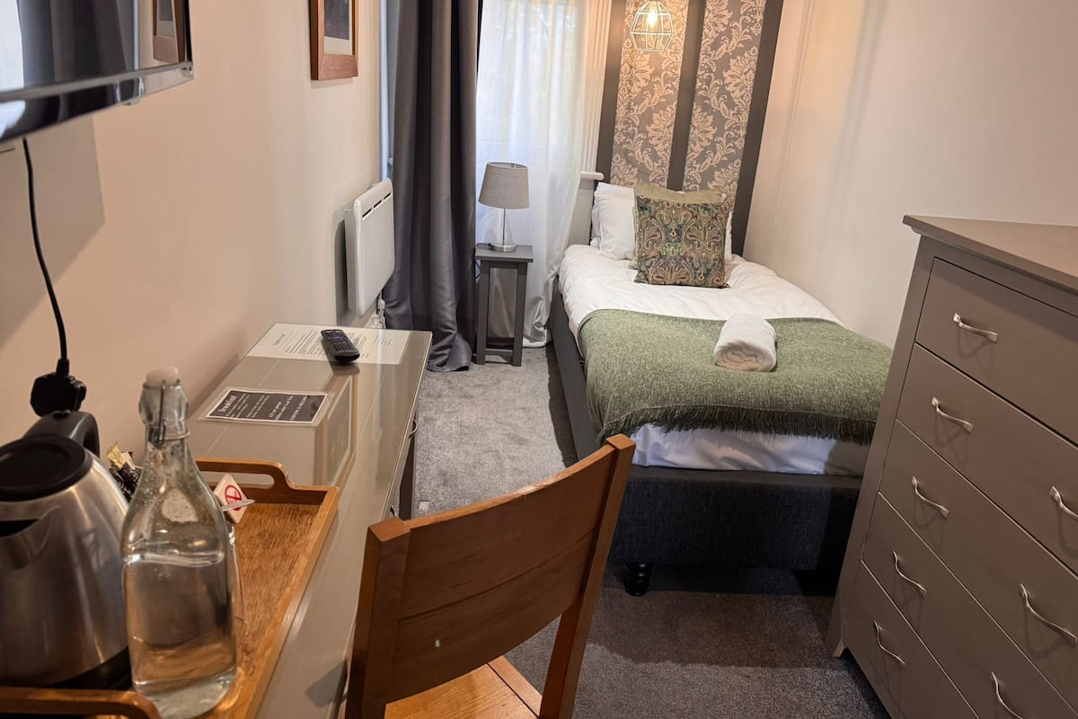 Una habitación de hotel con cama, escritorio con computadora portátil, silla, cómoda y radiador.