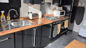 A modern kitchen with a wooden countertop, stainless steel sink, and black cabinets. - Regency Guest House (Cambridge)