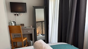 A hotel room with a bed, a desk, a chair, a television, and a window with curtains. - Regency Guest House (Cambridge)