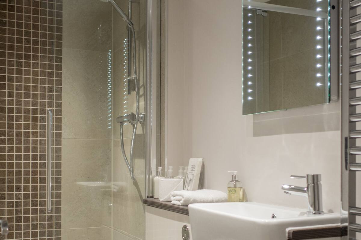 Un baño moderno con ducha envuelta en vidrio, un lavamanos blanco y un espejo grande con iluminación.