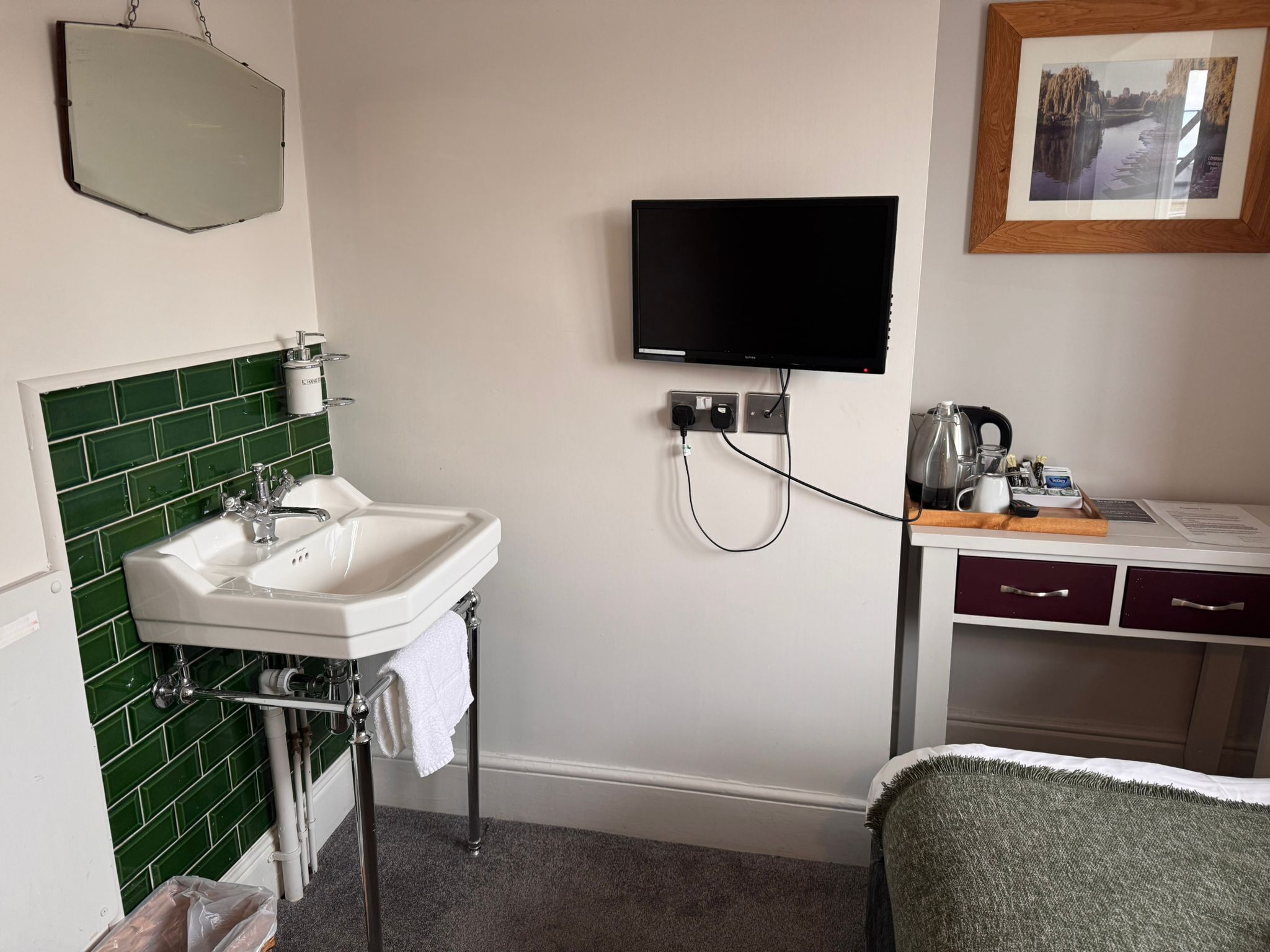 Un baño con lavamanos, espejo y televisión montada en la pared.