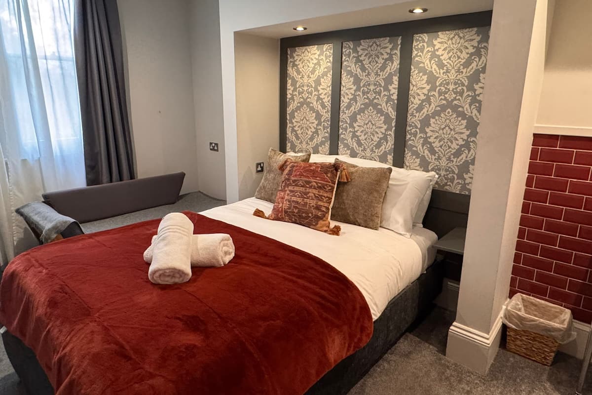 Una habitación de hotel con una cama grande, un cabecero con diseño estampado, una colcha roja y un pequeño banco.