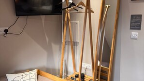A bedroom with a bed, a TV mounted on the wall, a wooden hanger stand, a mirror, and a red trash can. - Regency Guest House (Cambridge)