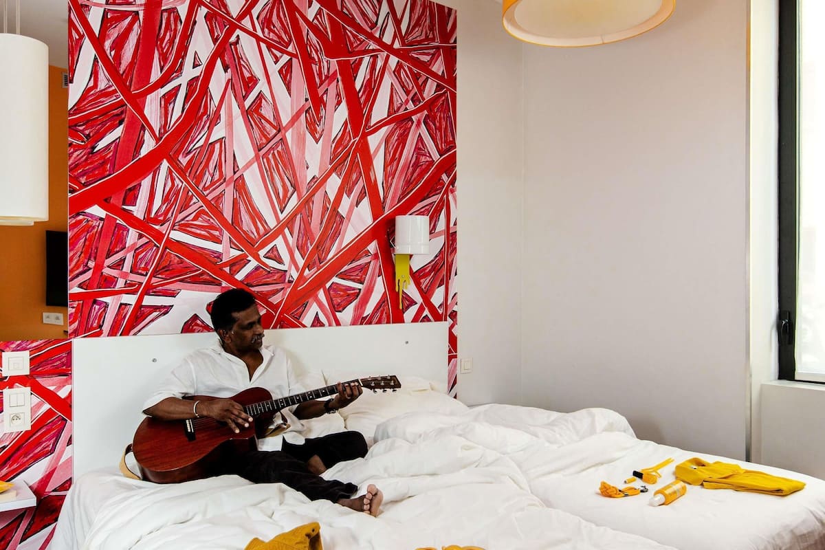 Una habitación con una cama, una guitarra y un diseño abstracto rojo y blanco en la pared.