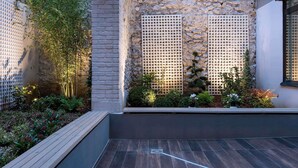 A courtyard with a stone wall, wooden deck, and a variety of plants. - ibis Styles Paris La Defense Courbevoie (Courbevoie)