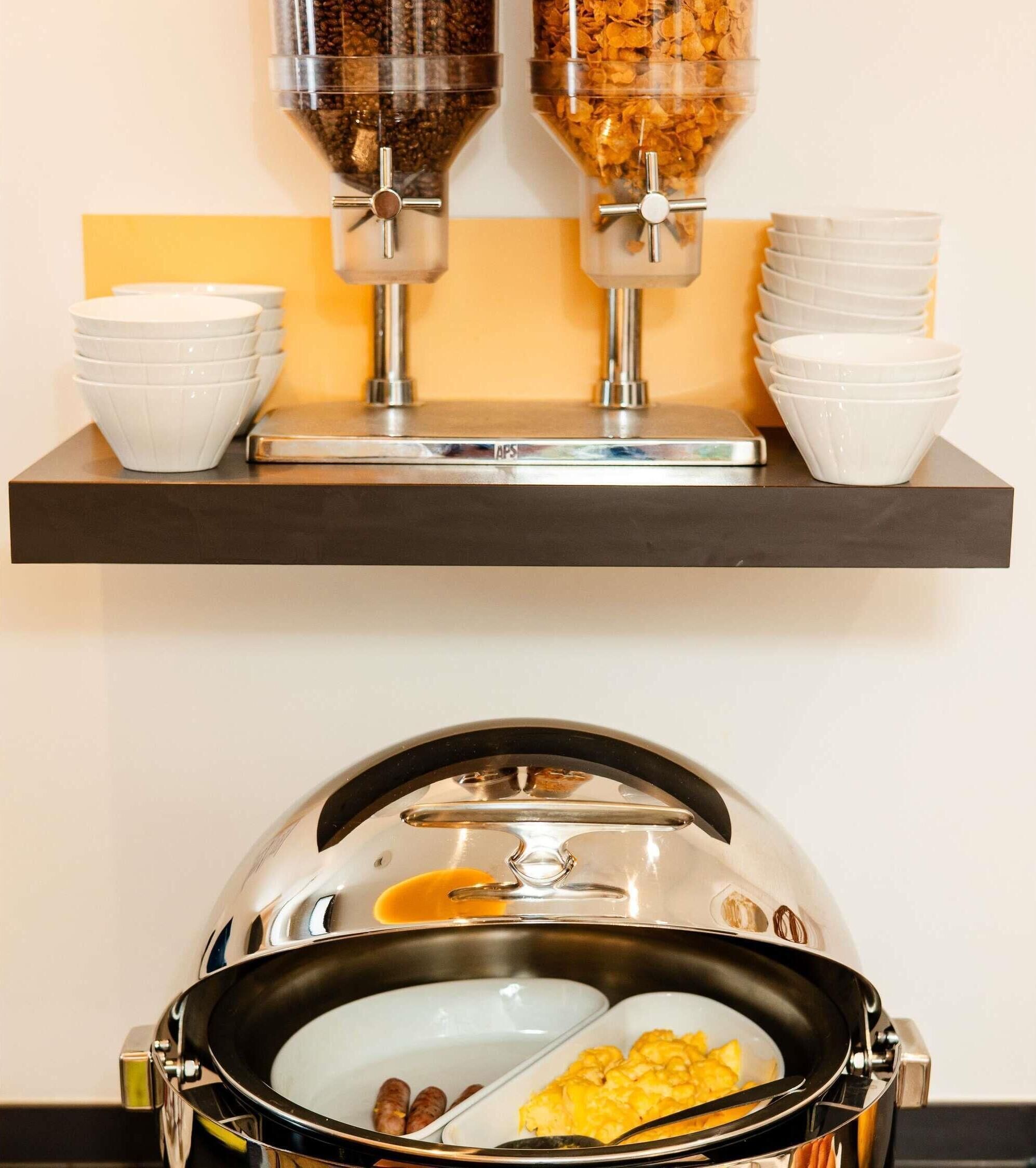 A buffet setup with a coffee dispenser, bowls, and a covered food station.