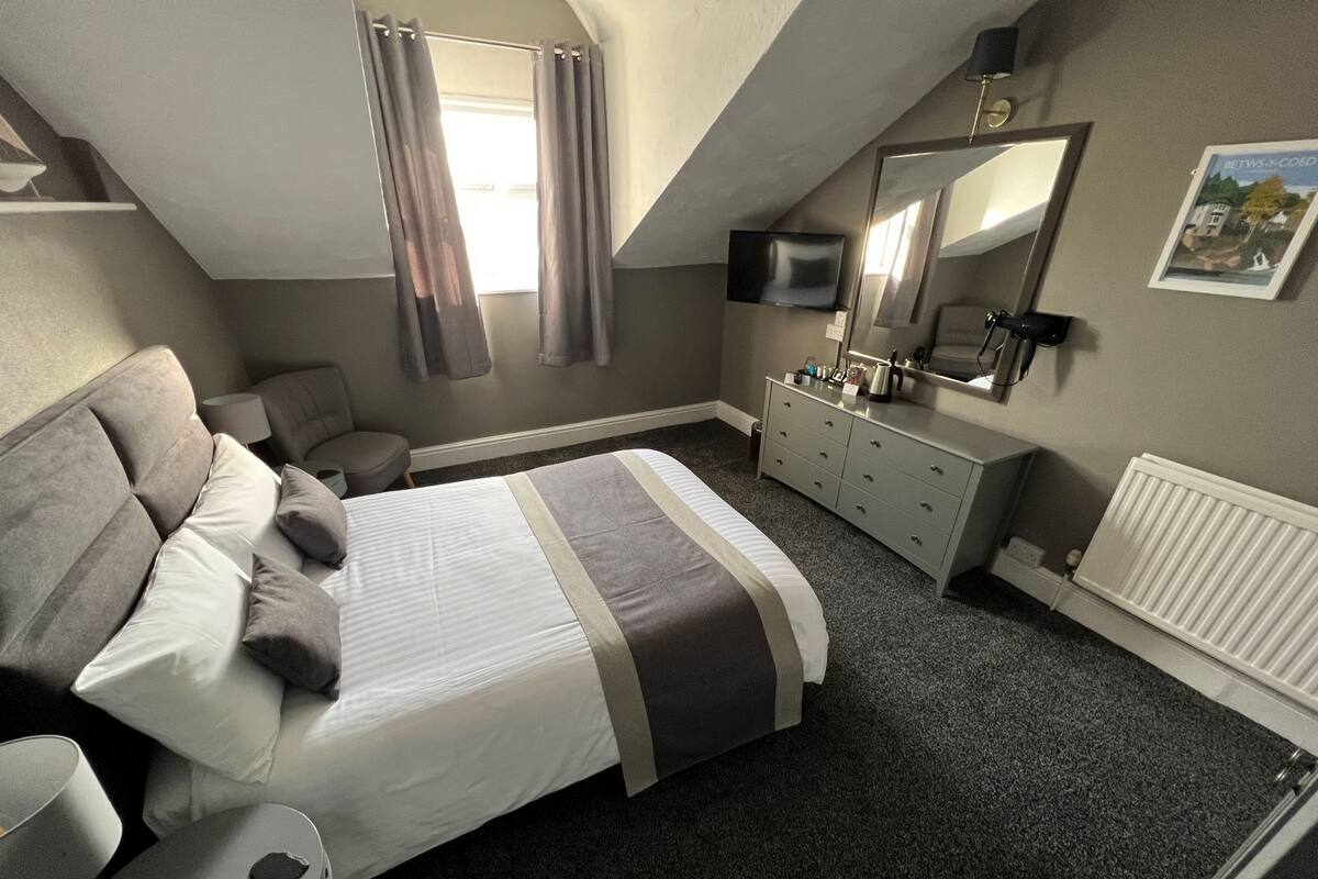 A bedroom with a bed, a chair, a dresser, a TV, and a radiator.