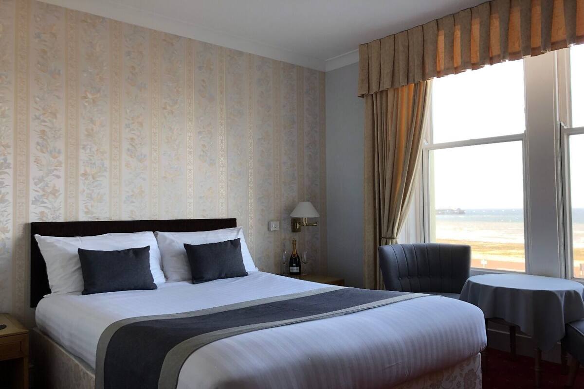 A hotel room with a large bed, a chair, a small table, and a view of the beach.