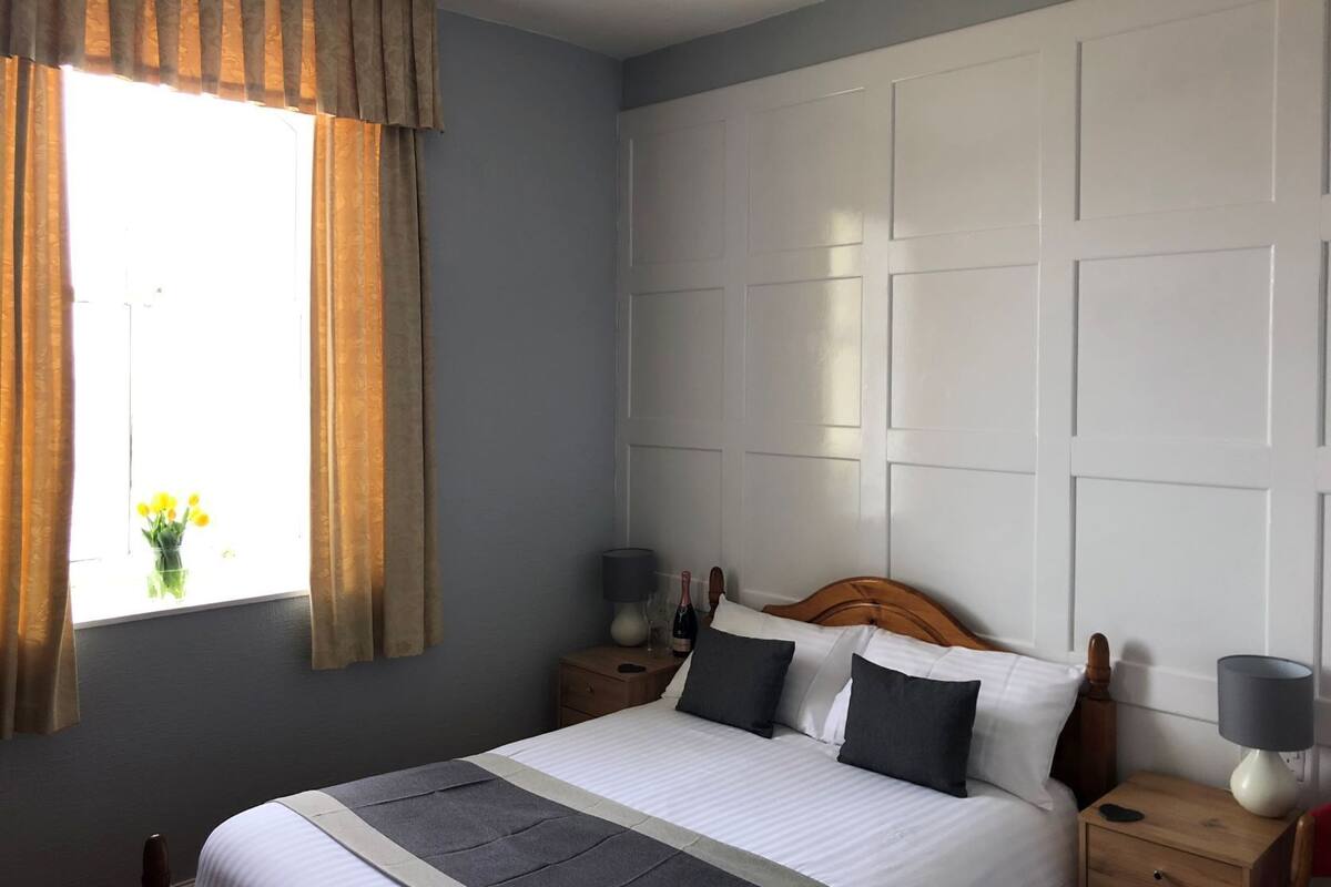 A neatly arranged bedroom with a bed, bedside tables, and a window with curtains.