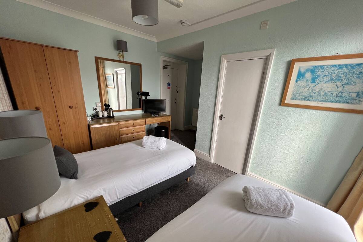 A hotel room with a bed, a desk, a mirror, a television, and a painting on the wall.