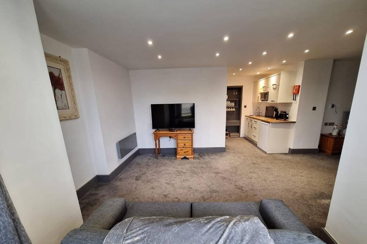 A living room with a grey sofa, a TV, and a kitchen in the background.
