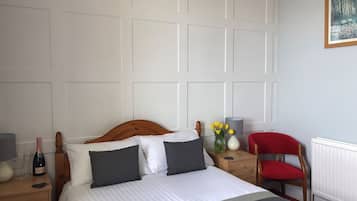 Un dormitorio ordenado con cama, mesitas de noche, una silla e imagen colgada en la pared.