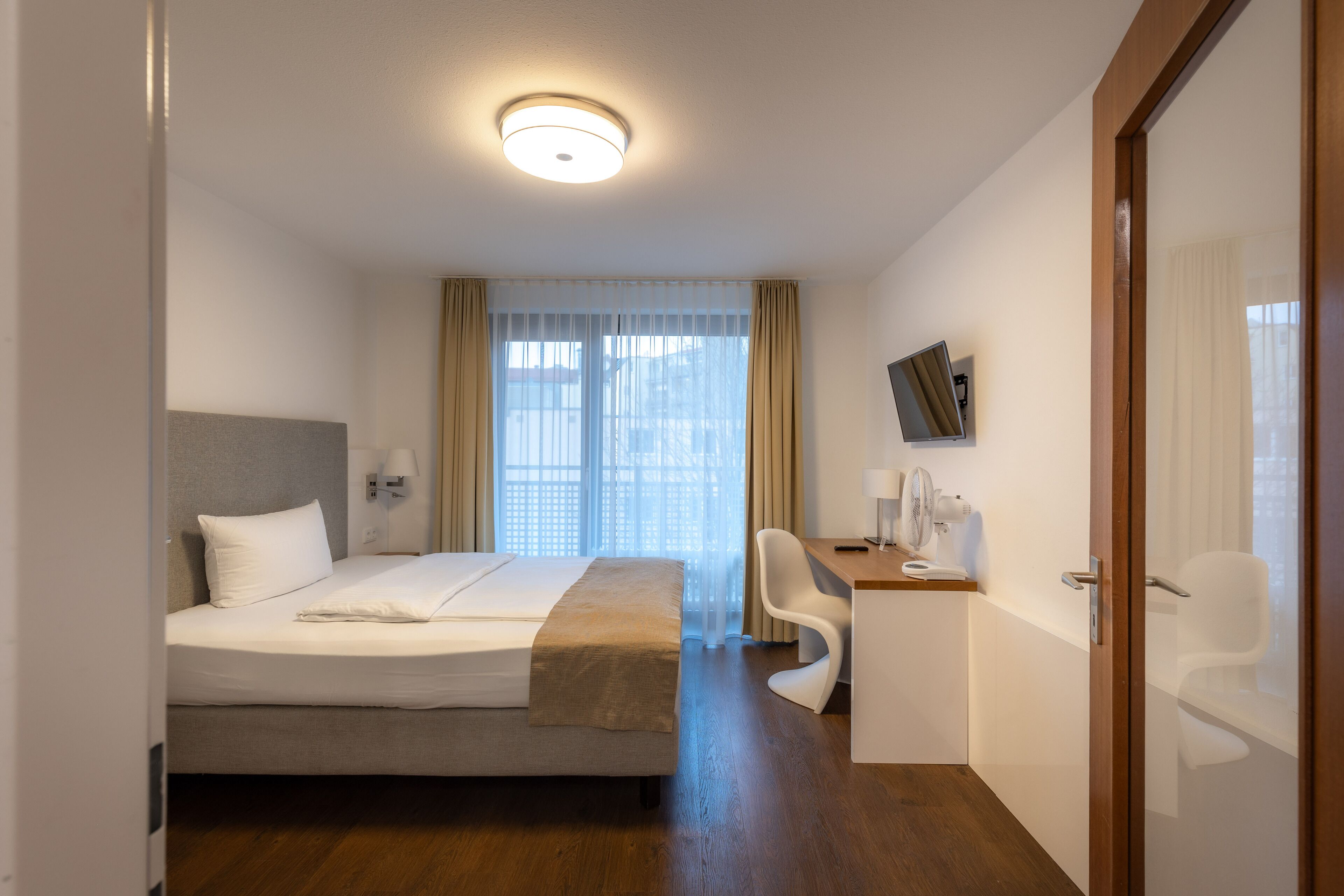 A hotel room with a bed, desk, chair, and a TV mounted on the wall.