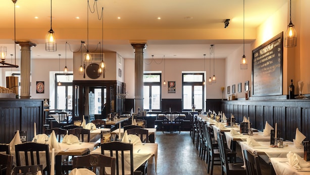 Un restaurant amb diverses taules i caires, llums penjants i un quadre de menú a la paret.