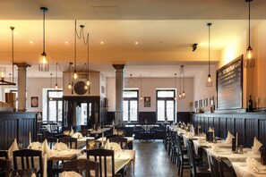A restaurant with multiple tables and chairs, hanging light fixtures, and a menu board on the wall. - Downtown Vi Vadi Hotel (Munich)