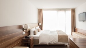 Una habitació d'hotel amb un llit gran, taules de nit, televisió i una finestra amb cortines.