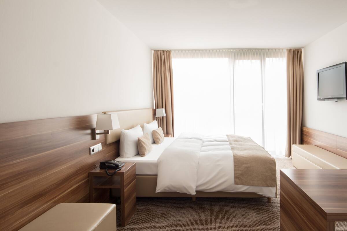 A hotel room with a large bed, bedside tables, a TV, and a window with curtains.