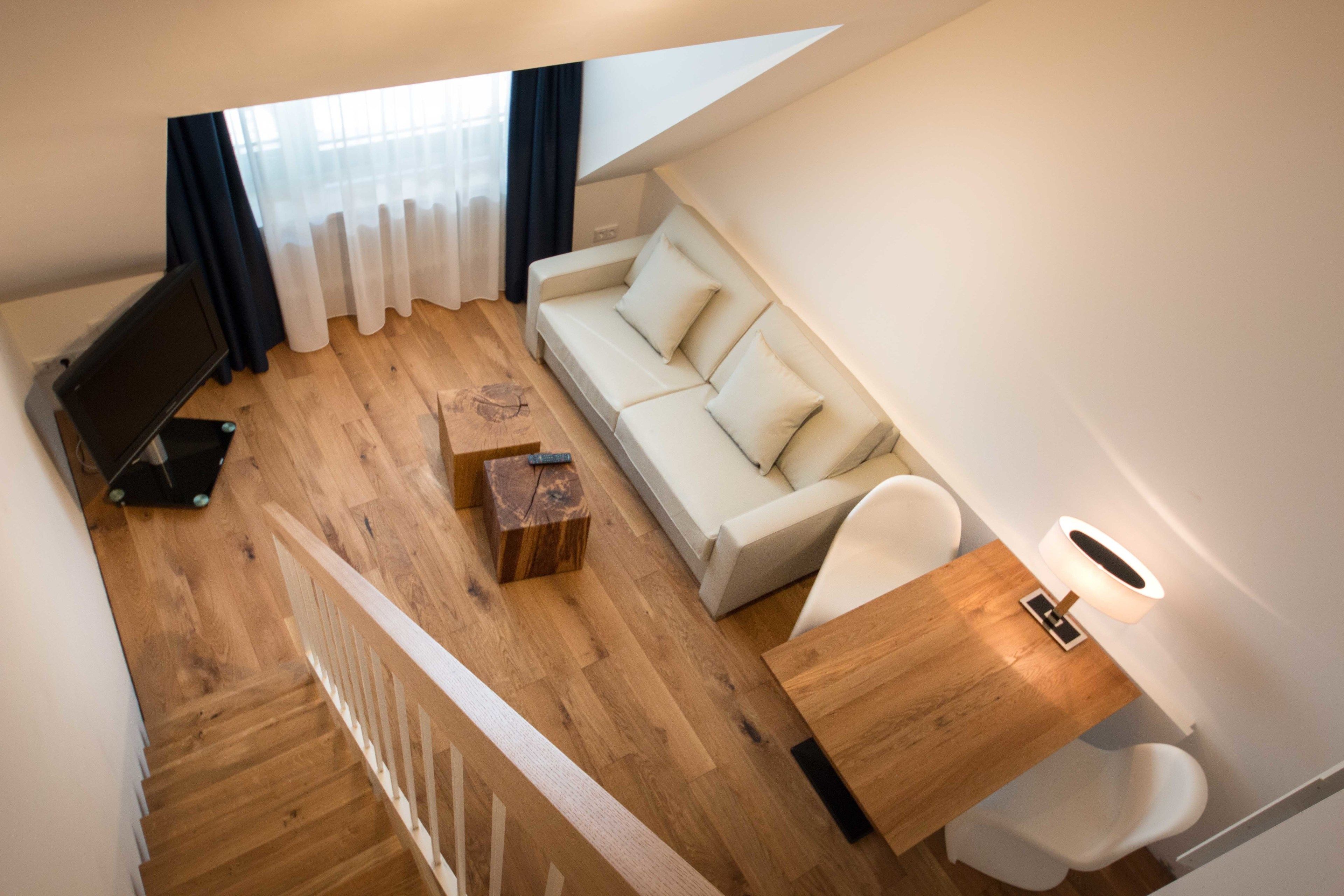A modern living room with a wooden floor, a white sofa, a small wooden coffee table, and a TV on a stand.