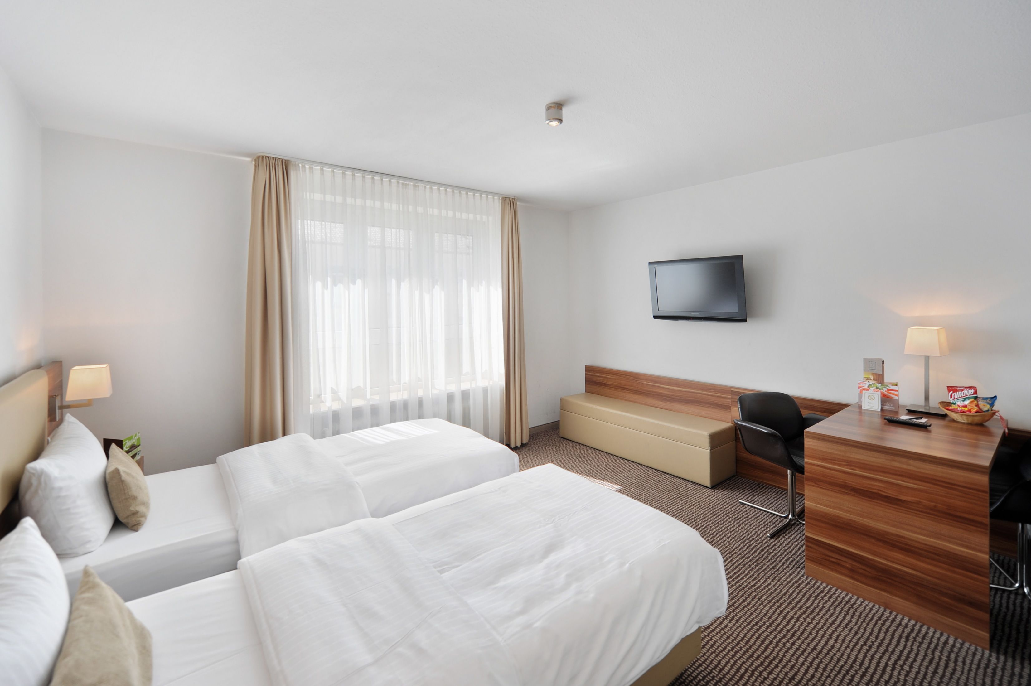 Habitación de hotel con dos camas, un escritorio, una silla, un televisor y una ventana con cortinas.