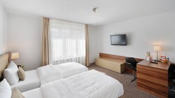 Habitación de hotel con dos camas, un escritorio, una silla, un televisor y una ventana con cortinas.