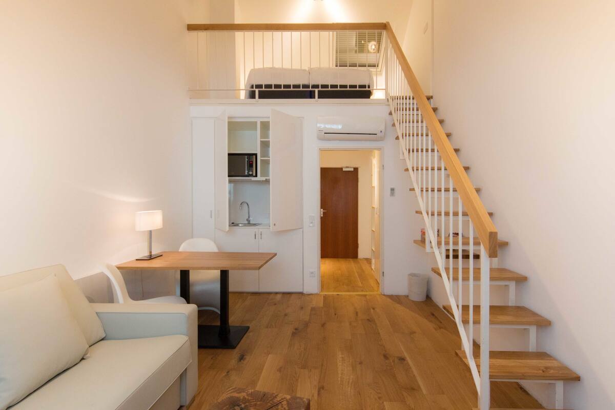 A compact living space with a loft bedroom, kitchenette, and a staircase.