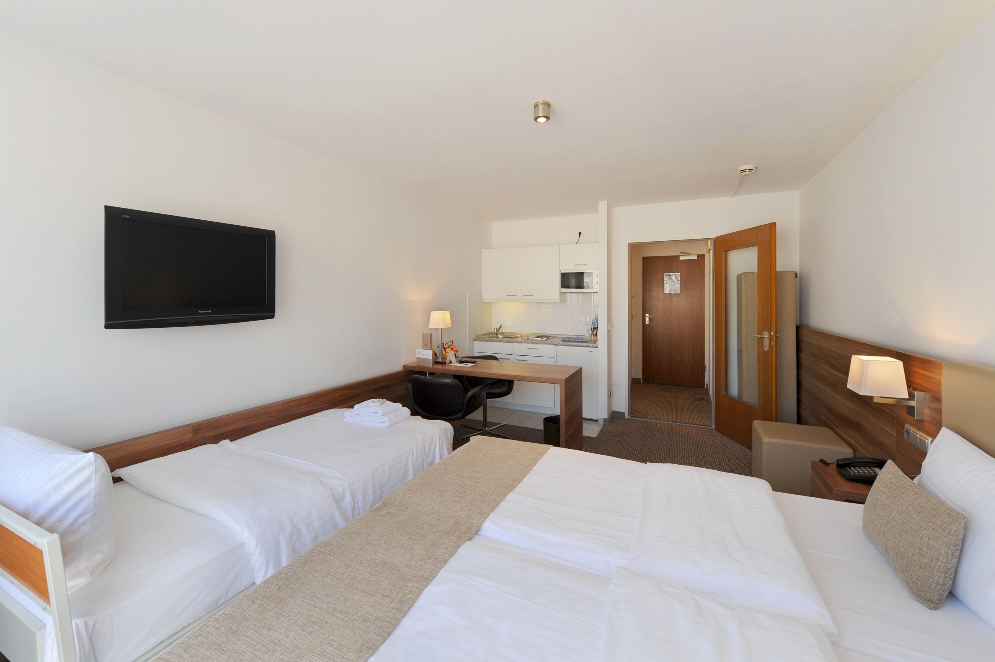 Una habitación de hotel con dos camas, un escritorio, televisor, microondas y pequeña cocina.