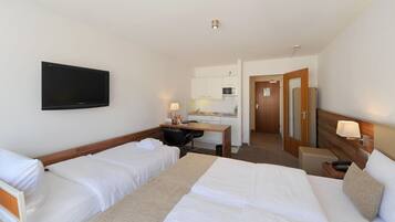 Una habitación de hotel con dos camas, un escritorio, televisor, microondas y pequeña cocina.
