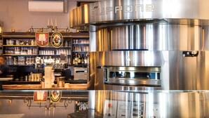 Un bar modern amb una màquina d'espresso d'acer inoxidable, prestatges amb gots i un taulell de bar polit.