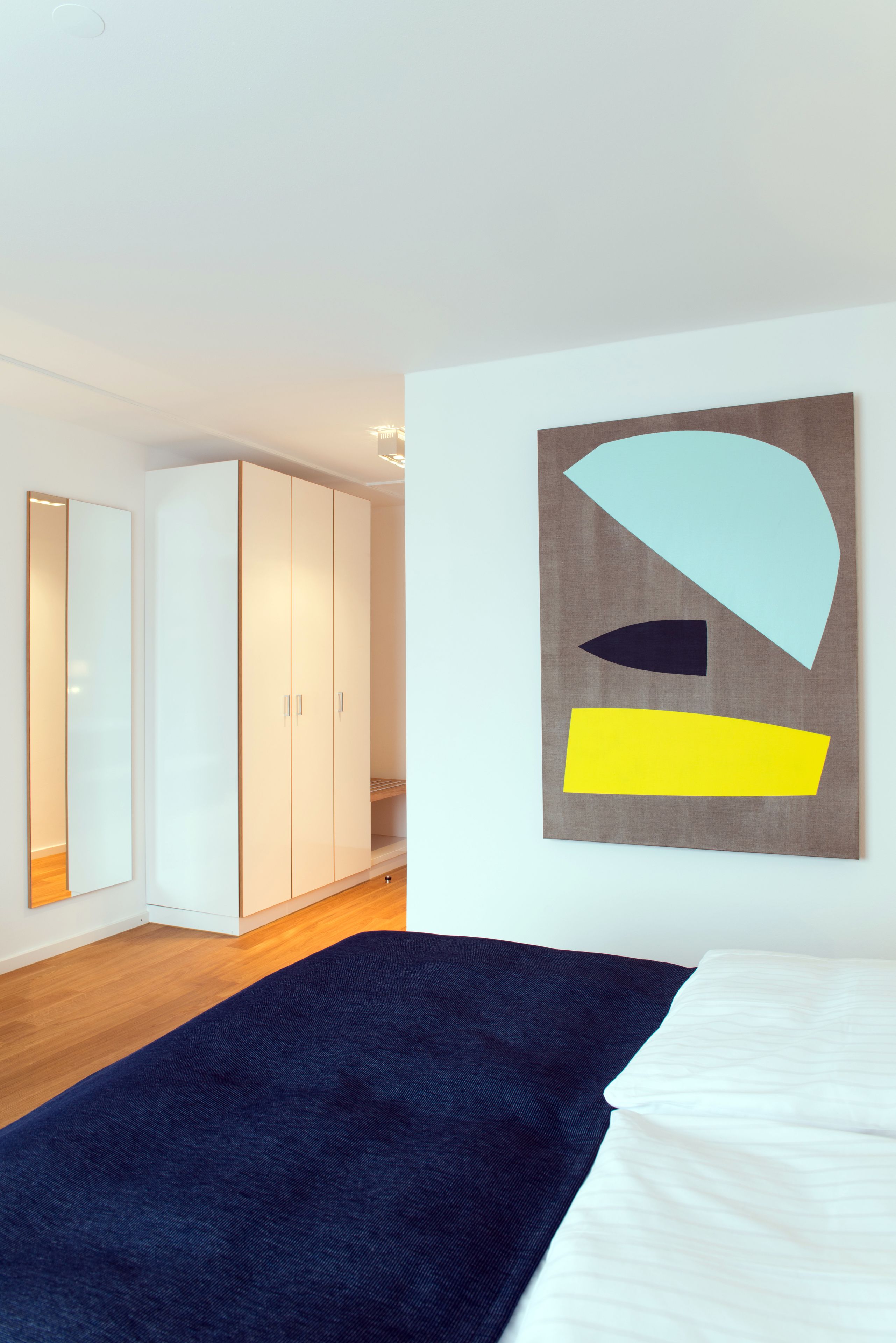 Un dormitorio con cama, armario y un cuadro abstracto grande en la pared.