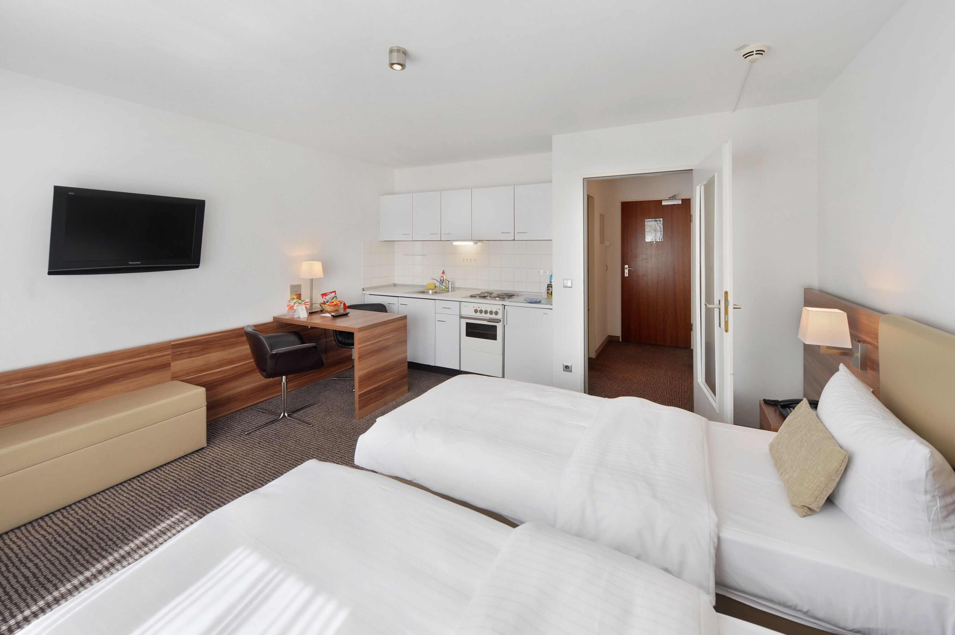 Una camera d'albergo con due letti, una scrivania, una televisione, un angolo cottura e un bagno.