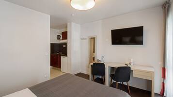 Habitación de hotel con cama, escritorio con dos sillas, televisión y una kitchenette al fondo.