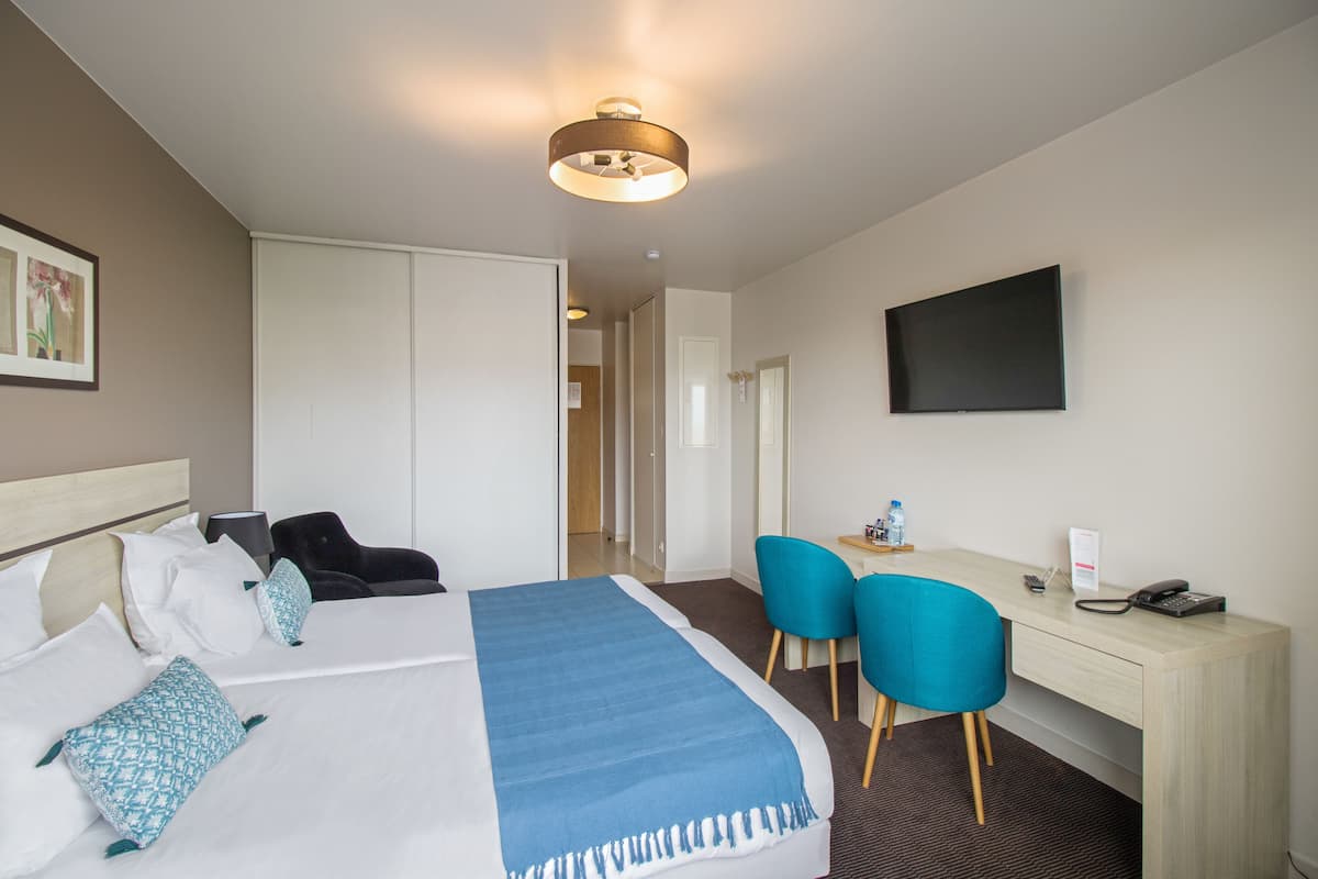 Habitación de hotel con cama, escritorio, dos sillas, televisor y puerta que da a otra habitación.