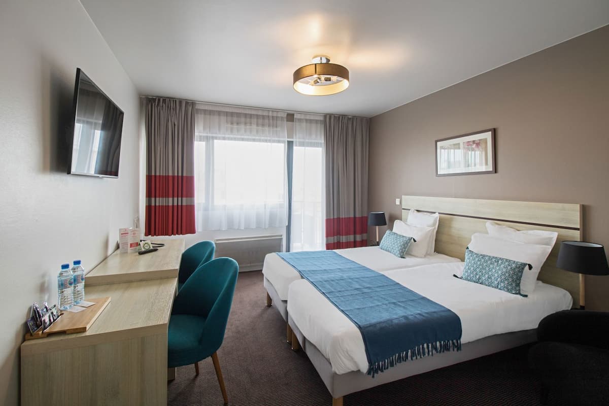 Habitación de hotel con cama, mesitas de noche, escritorio, sillas, televisor y ventana con cortinas.