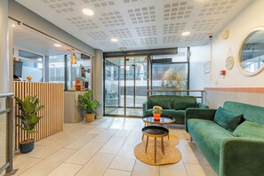 Un espace d’accueil avec un canapé vert, une table basse ronde et un comptoir de réception.