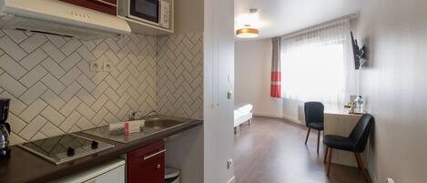 Cucina compatta con forno a microonde, piano cottura e lavello. C'è una zona pranzo con tavolo e sedie.