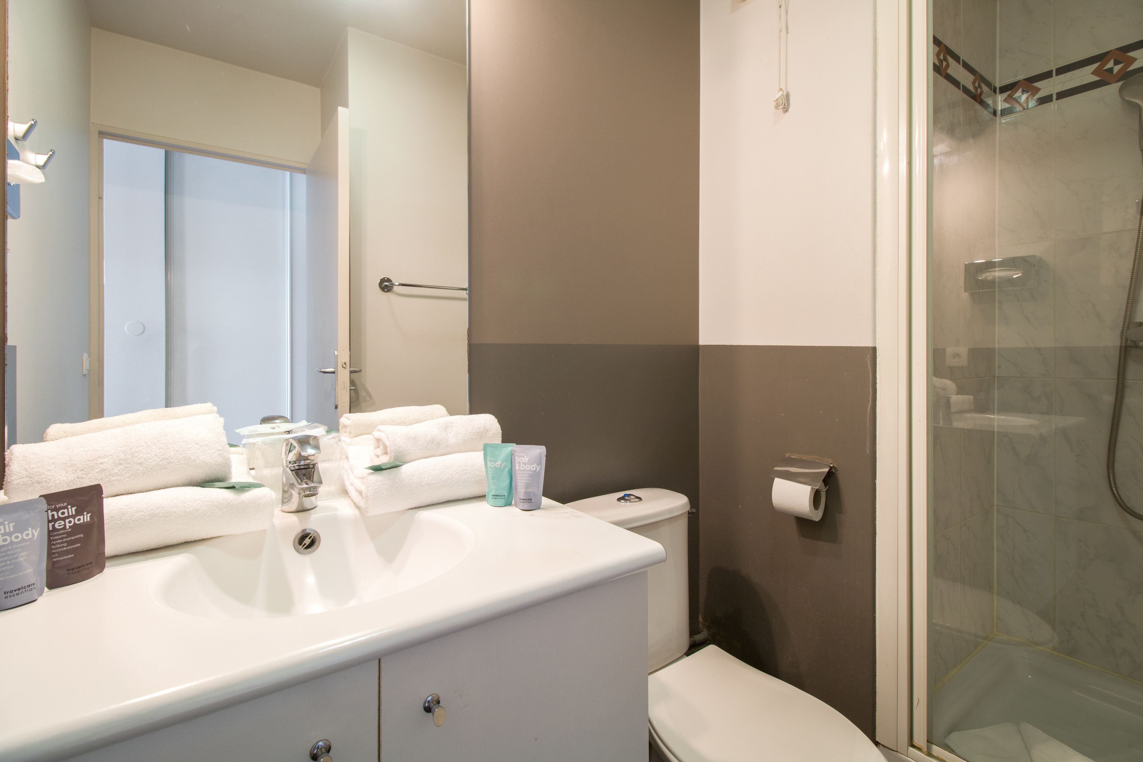 A bathroom with a sink, toilet, and shower. There are towels and toiletries on the sink.