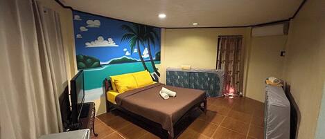A hotel room with a bed, a desk with a telephone, a small table with a lamp, and a wall mural.
