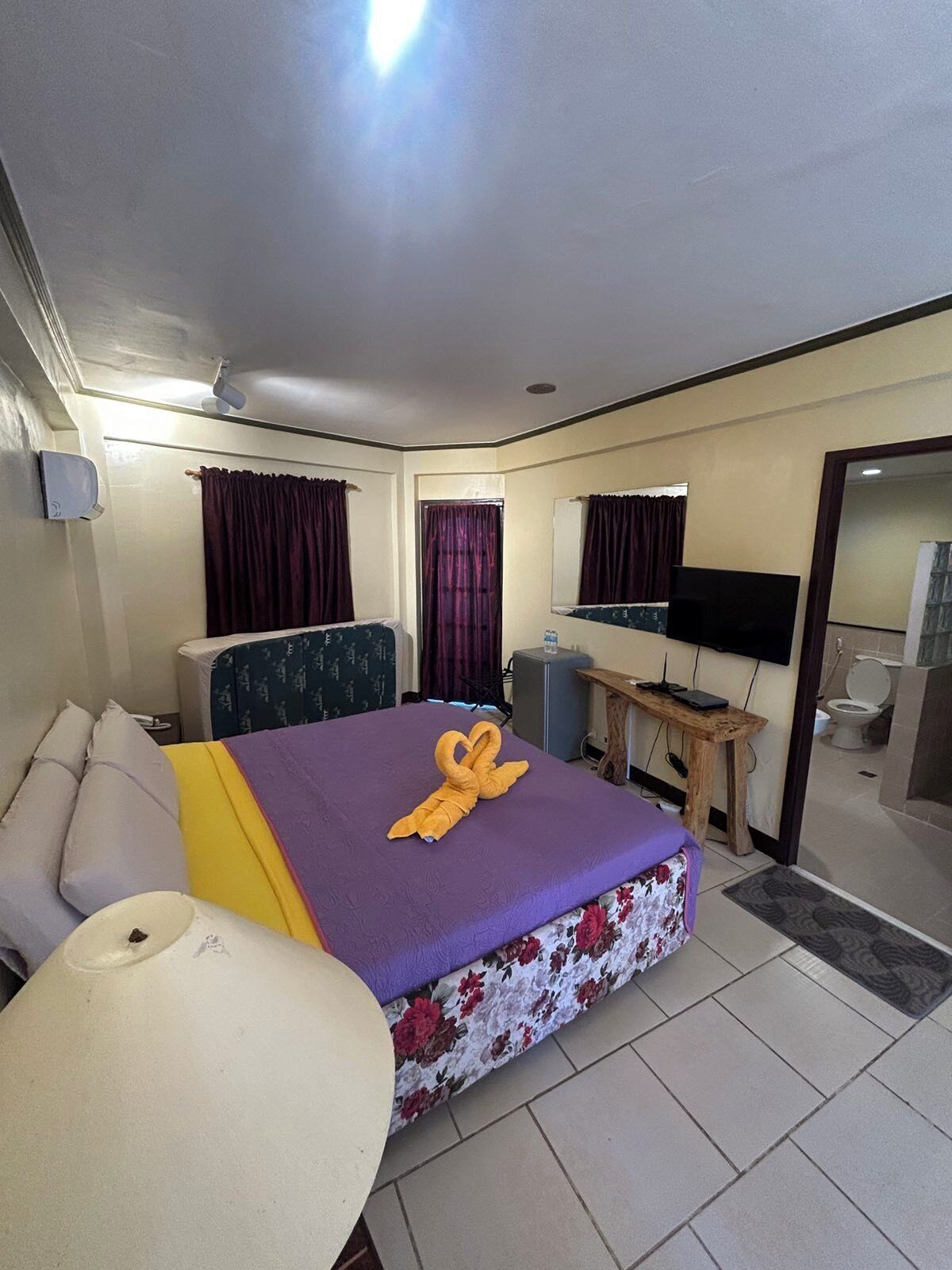 A hotel room with a bed, a desk, a TV, and a bathroom visible through an open door.
