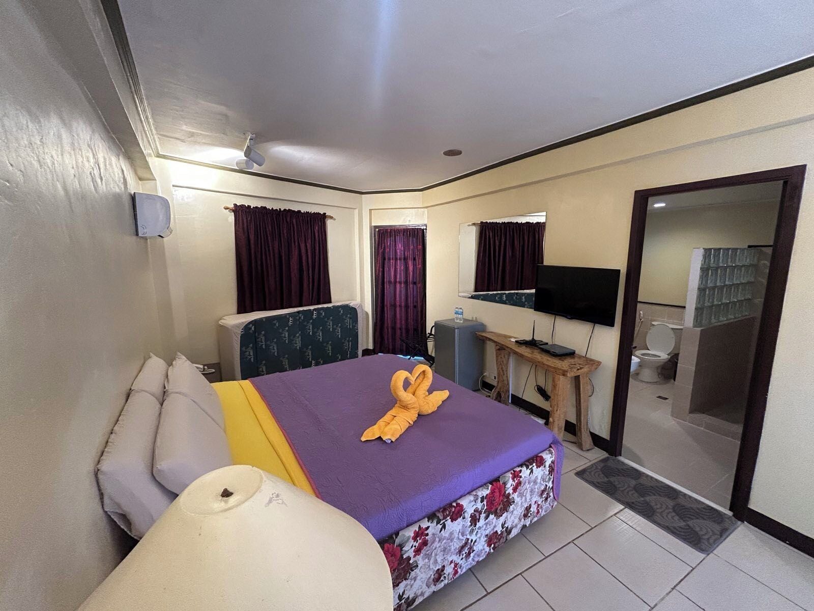 A hotel room with a bed, a desk, a television, and a bathroom visible through an open door.