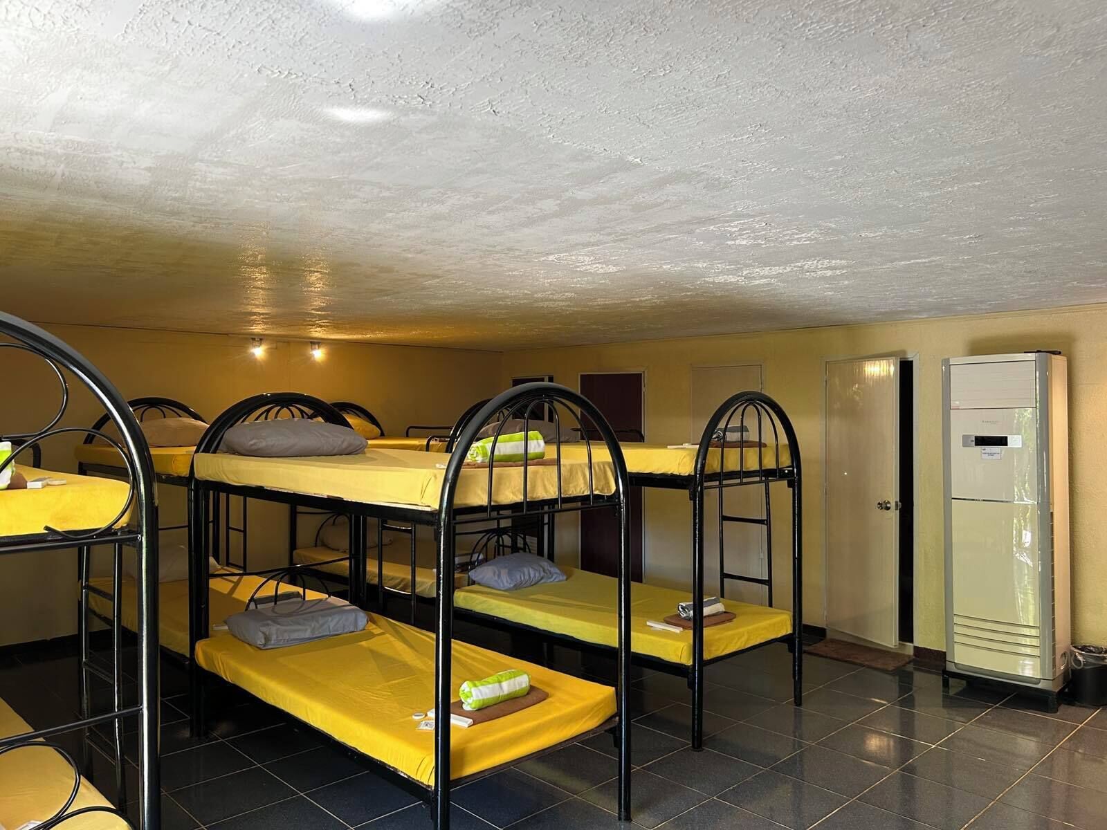 A dormitory room with bunk beds, a tiled floor, and a refrigerator.