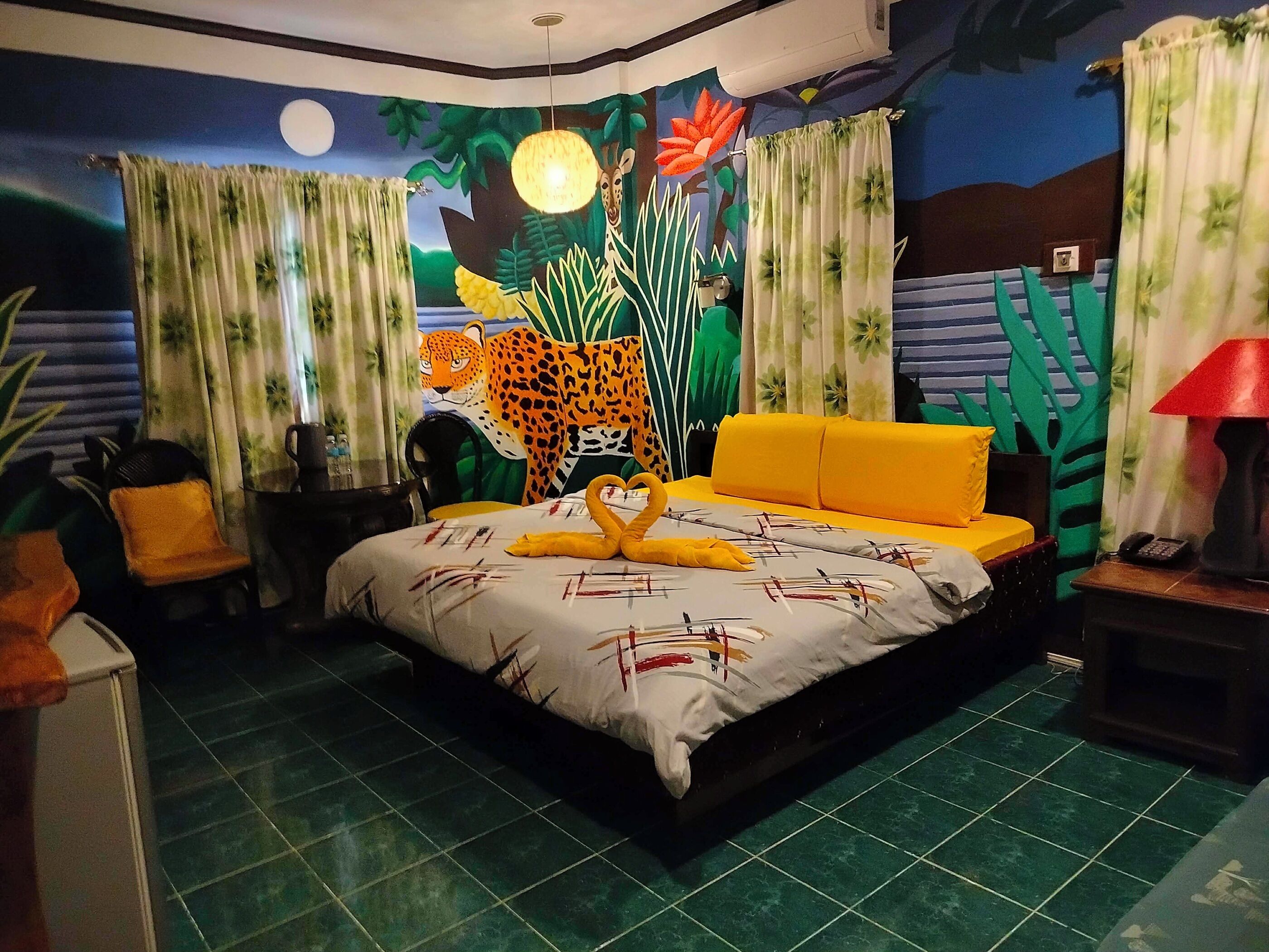 Una habitación con cama, mesita de noche, lámpara y un mural en la pared.