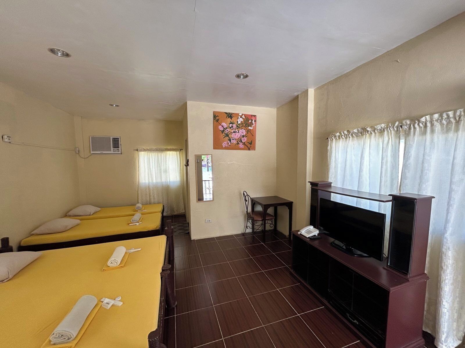 A hotel room with two beds, a television, a small table, and a painting on the wall.
