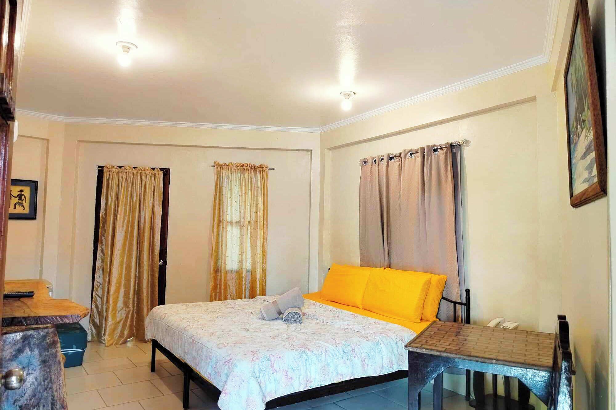 A bedroom with a bed, a desk, and curtains.