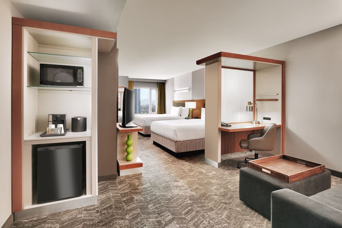 A hotel room with a kitchenette, a bed, a desk, and a view of the city.